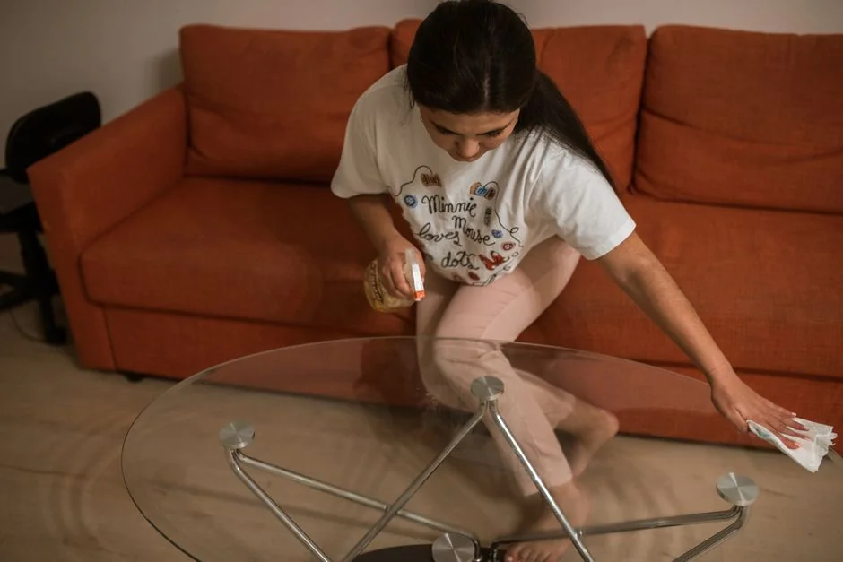 A woman carefully wraps a sofa in protective material while packing boxes in a bright room.